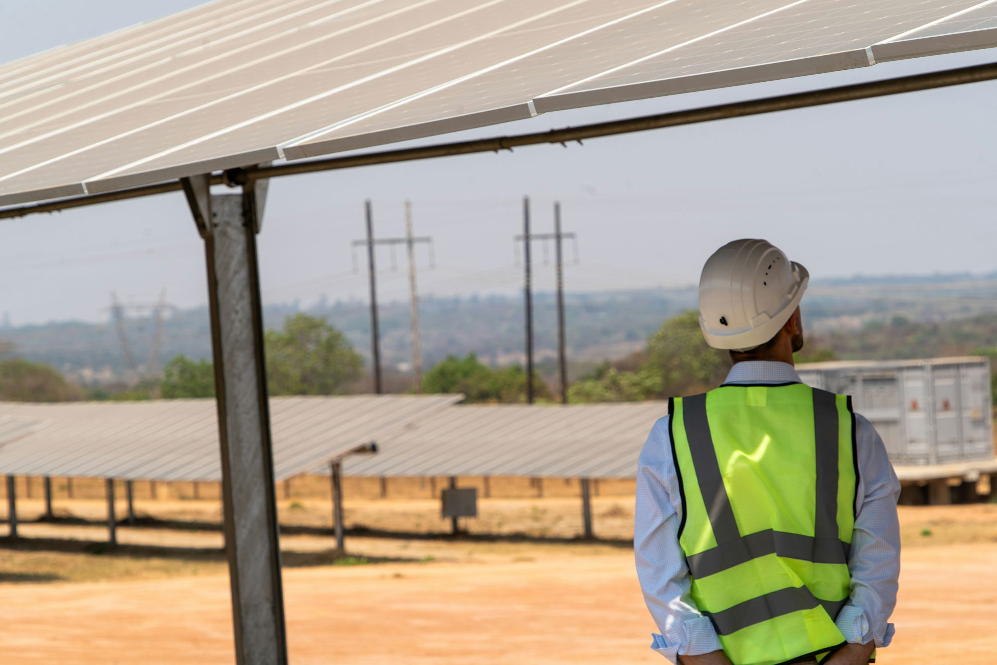 a-man-in-a-safety-vest-standing-under-a-solar-panel.jpg A man in a safety vest standing under a solar panel